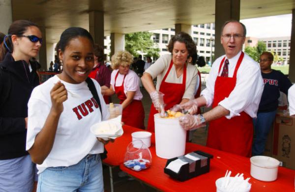 An older man and woman wearing red aprons scoop ice cream for a smiling student