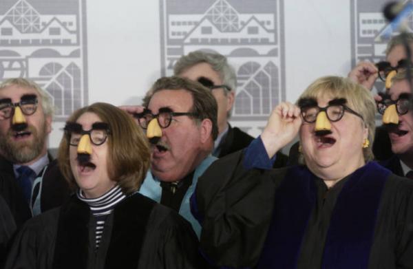 Seven people in fake glasses, noses and mustaches singing