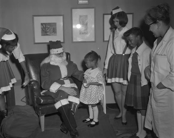 Man dressed as Santa Clause talking to small child. Four other people observe