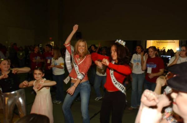 Two young woman in red dancing emphatically surrounded by other people