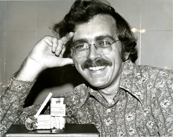 Man looking into the camera with rolls of cigarettes posed on the table he is leaning on