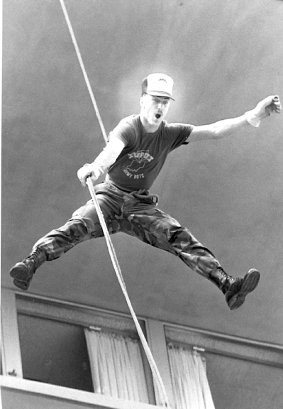 Young man with arms and legs splayed in the air and an exaggerated espression holds onto a rope high in the air