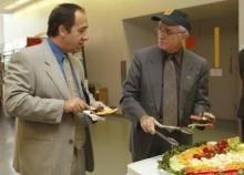 two older men in suits talking over a fruit spread