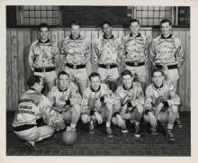 Ten young men in shiny jackets posing for a photo with a basketball in front of them