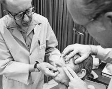 Two old men in lab coats manipulate a dummy's head