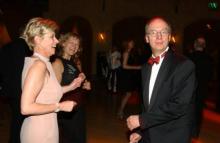 Two older women and an older man dance in a dark room. The man is looking into the camera