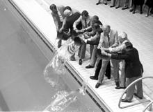 A group of men in suits throw buckets of water into a pool