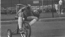 Young person leans over in a comical fashion while riding a tricycle