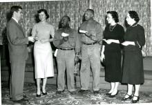 Five people holding slips of paper looking at a sixth man in a suit