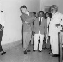 A group of men watching another man that is barely visible. One of the men is looking into the camera instead