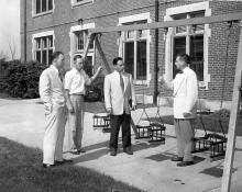 Four men stand talking arund a small swingset