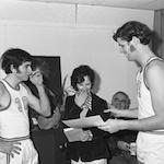 Woman looking at paper held between two basketball players.